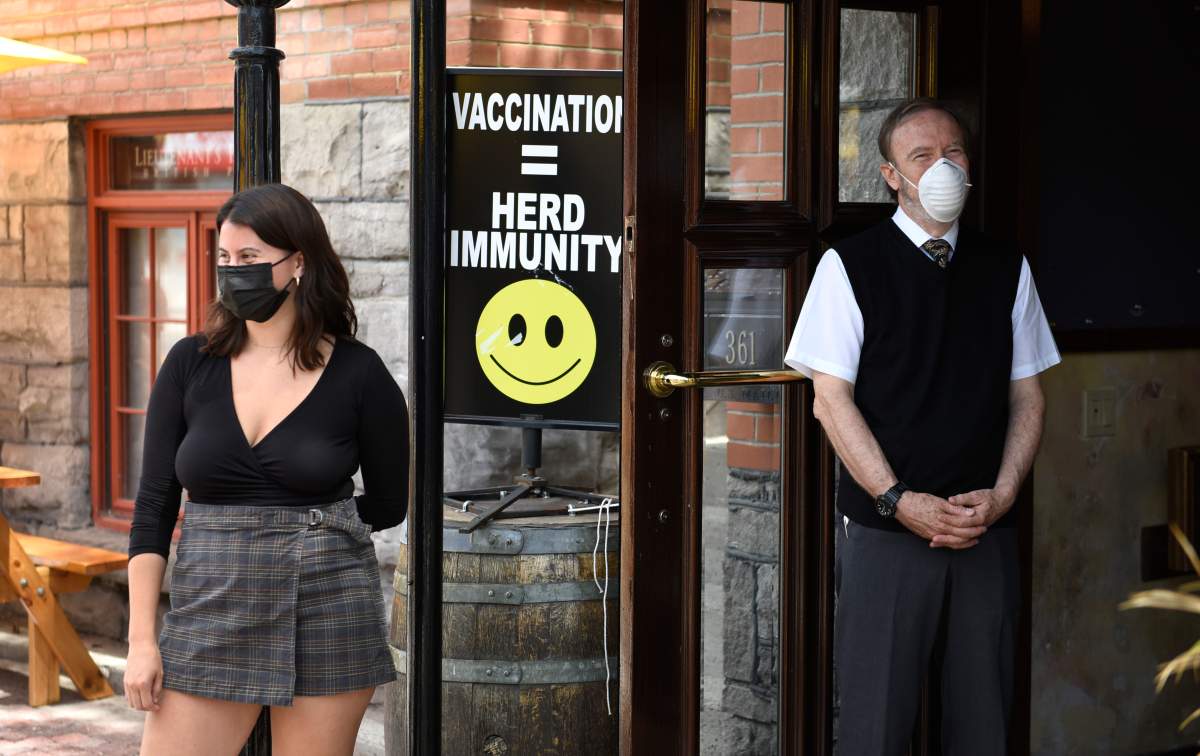 A sign encouraging vaccination is seen at the doors of a pub as staff watch patrons arrive, in Ottawa on the first day of Ontario's first phase of re-opening amidst the third wave of the COVID-19 pandemic, on Friday, June 11, 2021.