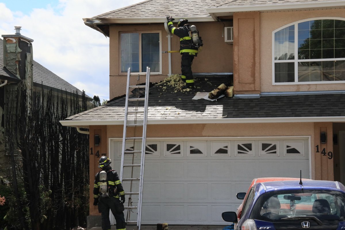 Firefighters inspect soffits of a house along Wyndham Crescent in Glenmore following a hedge fire on Saturday.