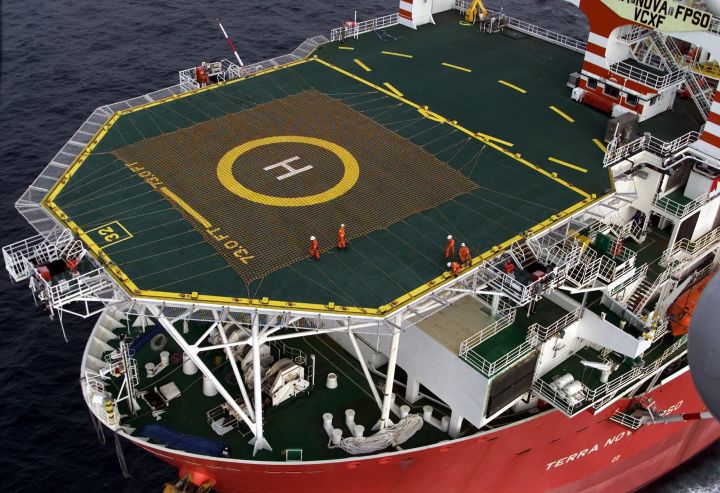 Workers stand on the helicopter landing pad on Terra Nova FPSO, a massive floating production, storage and offloading vessel used in the oil and gas industry, as it heads along the Newfoundland coast on Friday, Aug. 3, 2001. The $2.9 billion vessel, which stands 14 stories tall, will be used off the Newfoundland coast in the province's second major offshore project.
