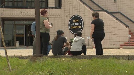 People sit outside the New Victory Church in southwest Calgary following a stabbing.