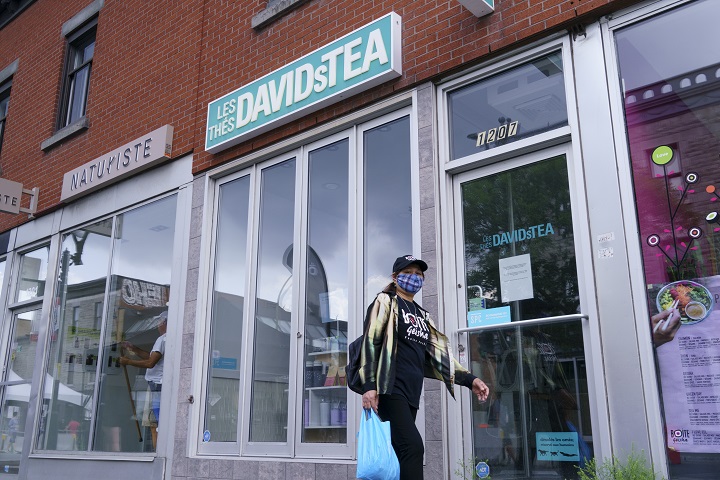A woman wearing a protective mask walks past a closed DavidsTea store in Montreal on Wednesday, July 8, 2020.