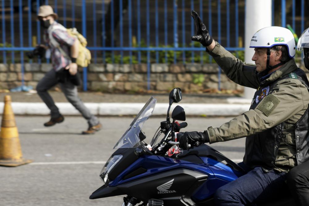 Brazil's President Jair Bolsonaro, waves as he leads a caravan of motorcycle enthusiasts following him through the streets of the city, in a show of support for Bolsonaro, in Sao Paulo, Brazil, Saturday, June 12, 2021.