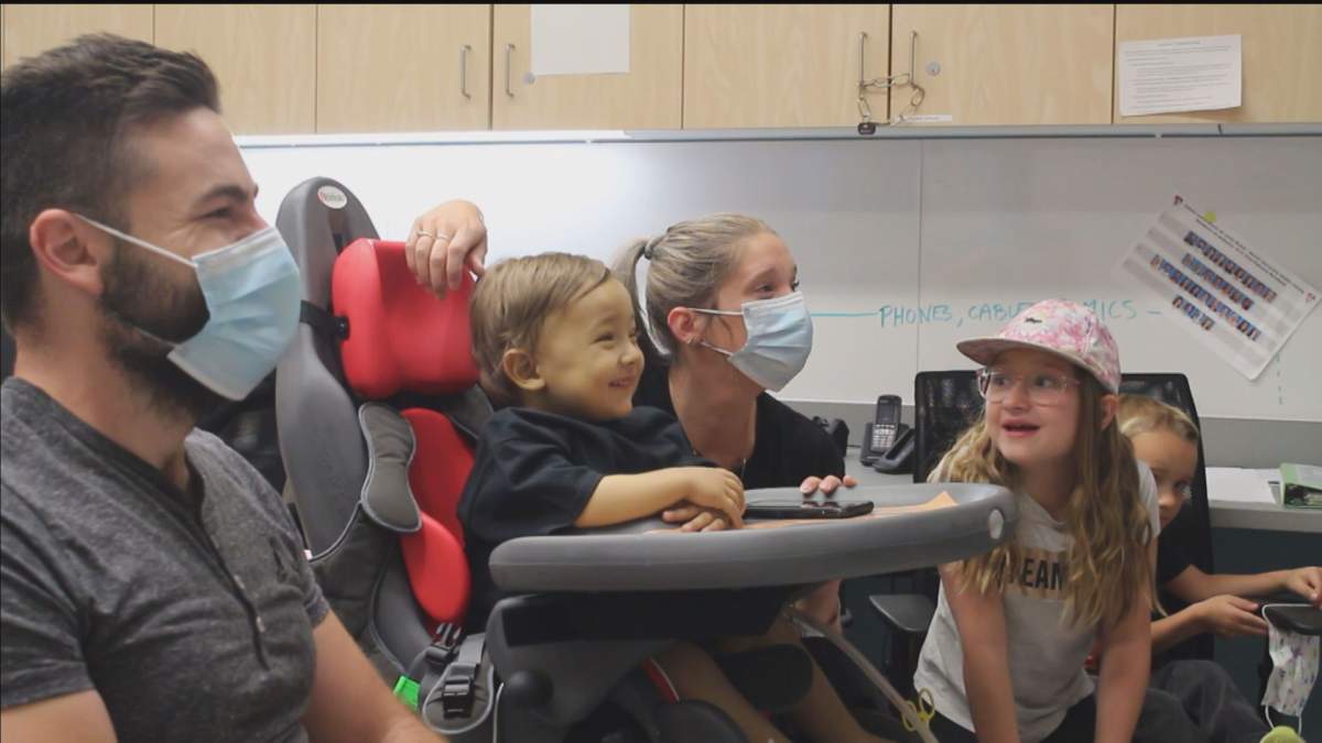 Milan sitting between his mom and dad smiles during a video chat with Metallica drummer Lars Ulrich.
