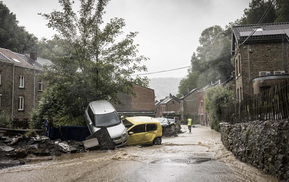 A man walks by damaged cars in a flooded street in Mery, Province of Liege, Belgium, Wednesday, July 14, 2021. A code red was issued in parts of Belgium on Wednesday as severe rains hit the area.