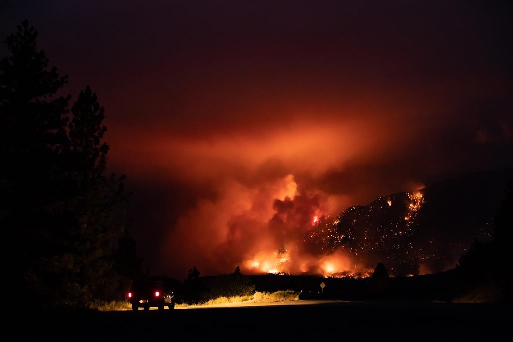 A motorist watches from a pullout on the Trans-Canada Highway as a wildfire burns on the side of a mountain in Lytton, B.C., Thursday, July 1, 2021. 