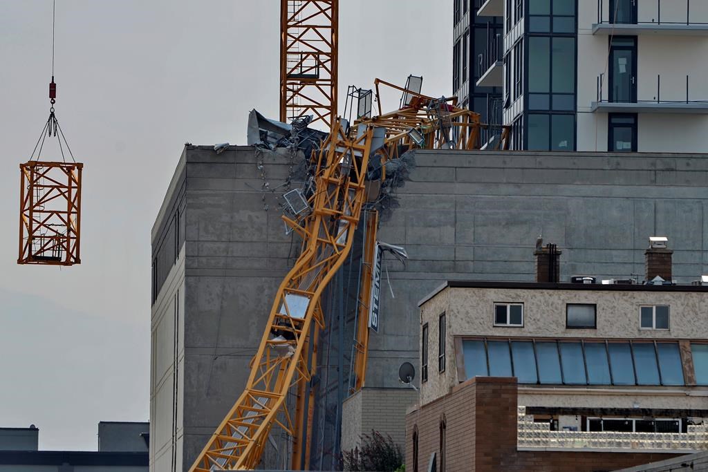 FILE. A section (left) of the vertical column of a construction crane is lowered past the mangled section of the fallen boom in Kelowna, B.C., Wednesday, July 14, 2021, following a fatal collapse of the crane.   