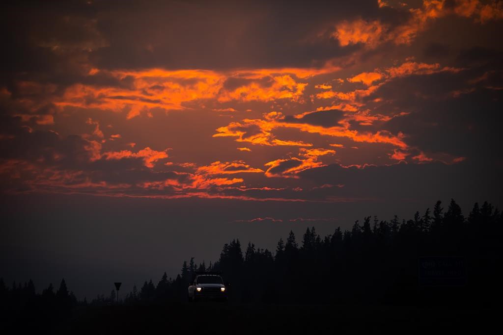 Smoke particles from wildfires enhance the colour of a sunset as a motorist travels on Highway 97C near Logan Lake, B.C., on Thursday, July 15, 2021. Above average temperatures for many parts of B.C. aren't expected to ease soon and Environment Canada says there is no hint of showers until at least the weekend for some regions of southern B.C. hit hard by wildfires. THE CANADIAN PRESS/Darryl Dyck.
