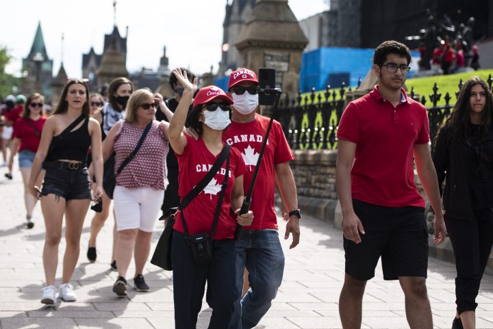 People wear the maple leaf as they wave into a camera phone as they walk along Wellington Street in Ottawa on Canada Day, Thursday, July 1, 2021. 
