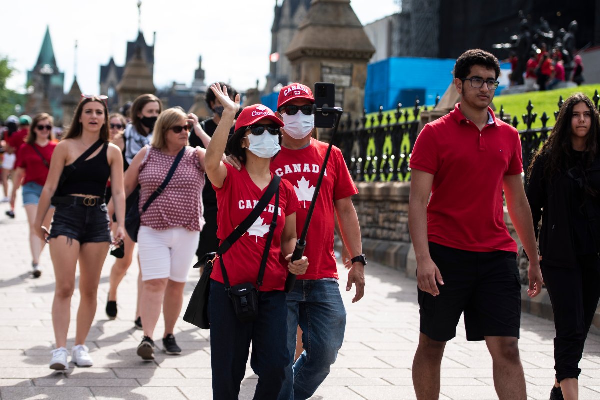 People wear the maple leaf as they wave into a camera phone as they walk along Wellington Street in Ottawa on Canada Day, Thursday, July 1, 2021. 