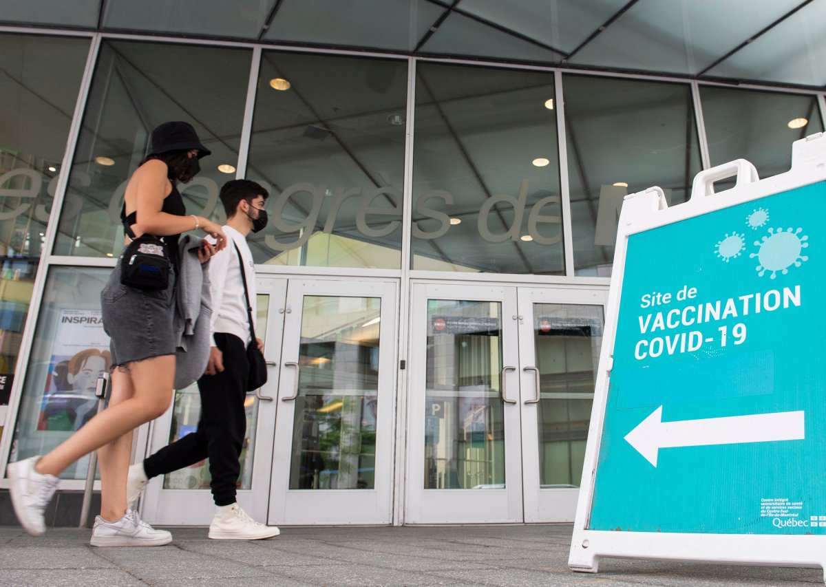 People wear face masks as they walk by a sign at a COVID-19 vaccination site in Montreal, Sunday, July 4, 2021. 