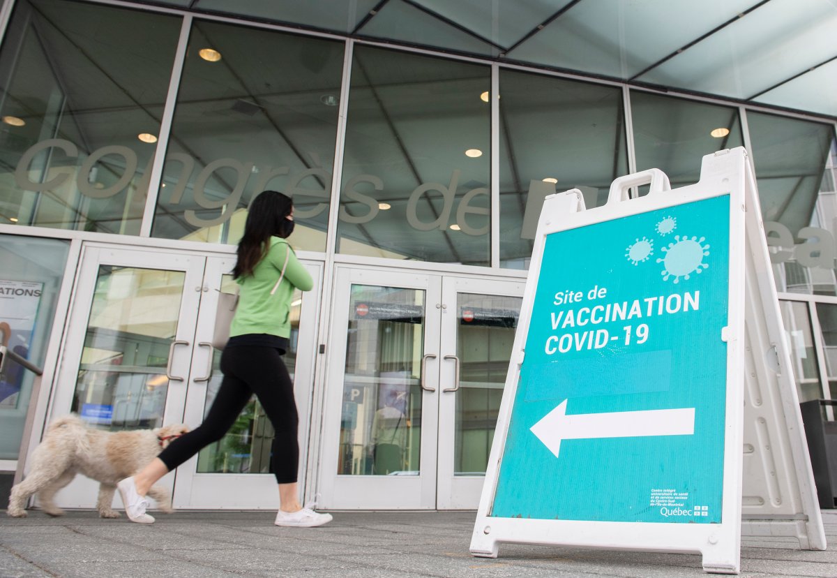 A woman and dog walk by a sign at a COVID-19 vaccination site in Montreal, Sunday, July 4, 2021. 