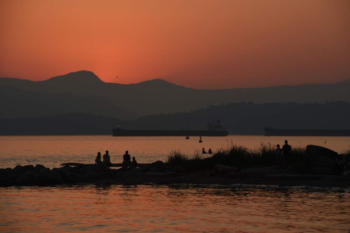 People are silhouetted as they watch the sunset along English Bay in Vancouver, British Columbia on a hot summer evening on June 29, 2021. 