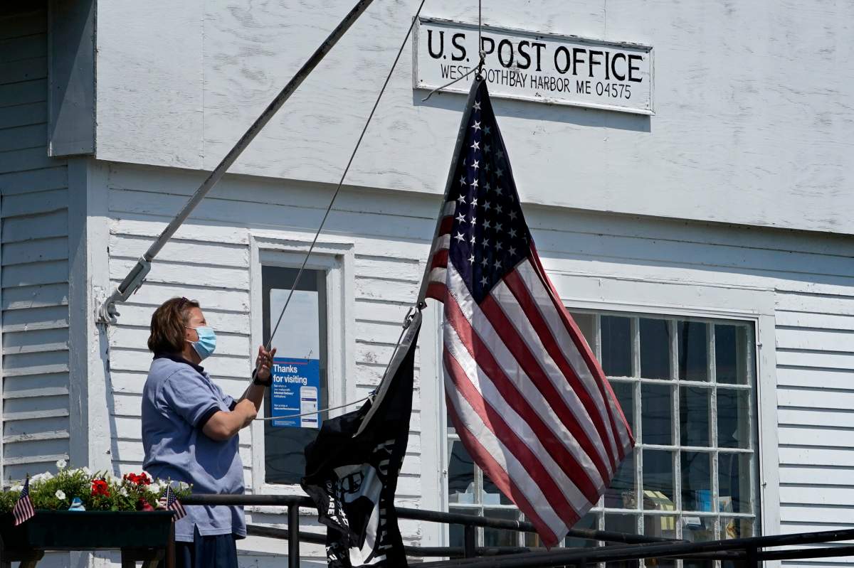 An employee raises the American flag outside a branch of the U.S. Post Office, Wednesday, July 7, 2021, in West Boothbay Harbor, Maine.