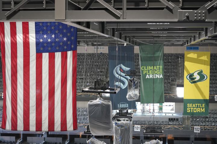 United States and team flags hang in the rafters of the Climate Pledge Arena during a media tour of the facility, Monday, July 12, 2021, in Seattle. The arena will be the home of the NHL hockey team Seattle Kraken and the WNBA Seattle Storm basketball team as well as hosting concerts and other performing arts events.
