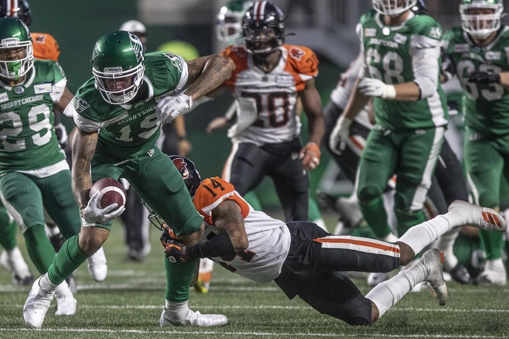 Saskatchewan Roughriders wide receiver Brayden Lenius (19) tries to break away from a tackle by BC Lions defensive back Marcus Sayles (14) during the first half of CFL football action in Regina on Friday, August 6, 2021. THE CANADIAN PRESS/Kayle Neis.