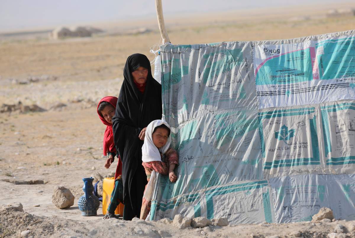 An internally displaced Afghan woman stands with her daughters in front a makeshift tent in a camp on a rocky patch of land, after fleeing fighting between the Taliban and Afghan security personnel, on the edge of the city of Mazar-e-Sharif, northern Afghanistan, Thursday, July 8, 2021. (AP Photo/Rahmat Gul)
