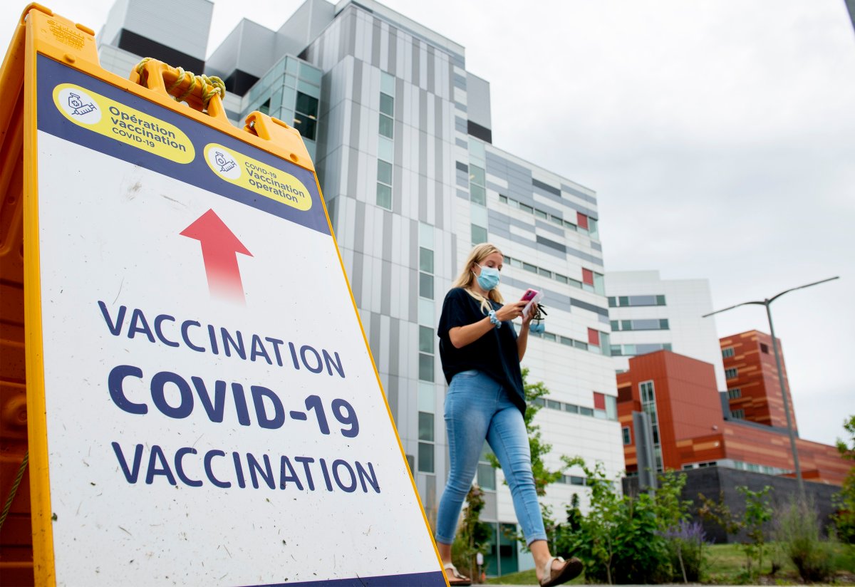 A woman wears a face mask as she walks by a COVID-19 vaccination sign in Montreal, Sunday, August 1, 2021, as the COVID-19 pandemic continues in Canada and around the world. 