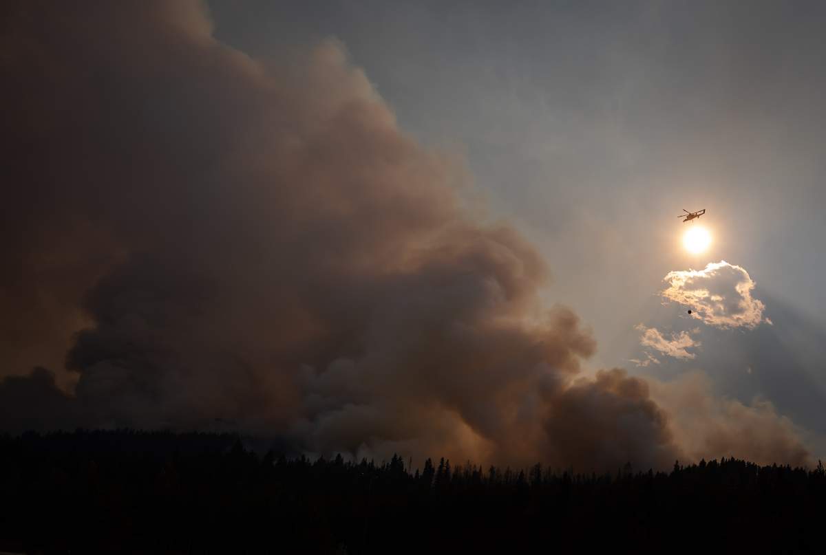 A helicopter with a water bucket flies past smoke rising into the air while battling the July Mountain wildfire along the Coquihalla Highway south of Merritt, B.C., on Wednesday, August 11, 2021. 