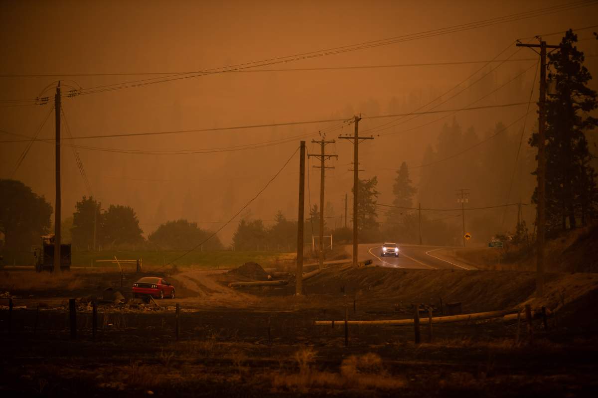 Thick smoke fills the air and nearly blocks out the sun just before 3 p.m. as a motorist on Highway 97 travels past an area burned by the White Rock Lake wildfire in Monte Lake, east of Kamloops, B.C., on Saturday, August 14, 2021. 