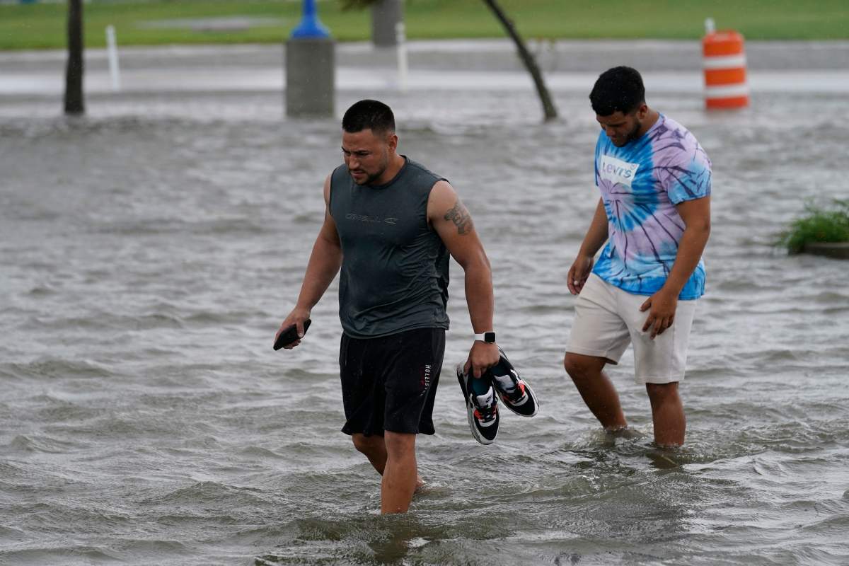 Jesse Perez, center, and Sergio Hijuelo walk through flooded streets near Lake Pontchartrain as Hurricane Ida nears, Sunday, Aug. 29, 2021, in New Orleans. (AP Photo/Gerald Herbert)