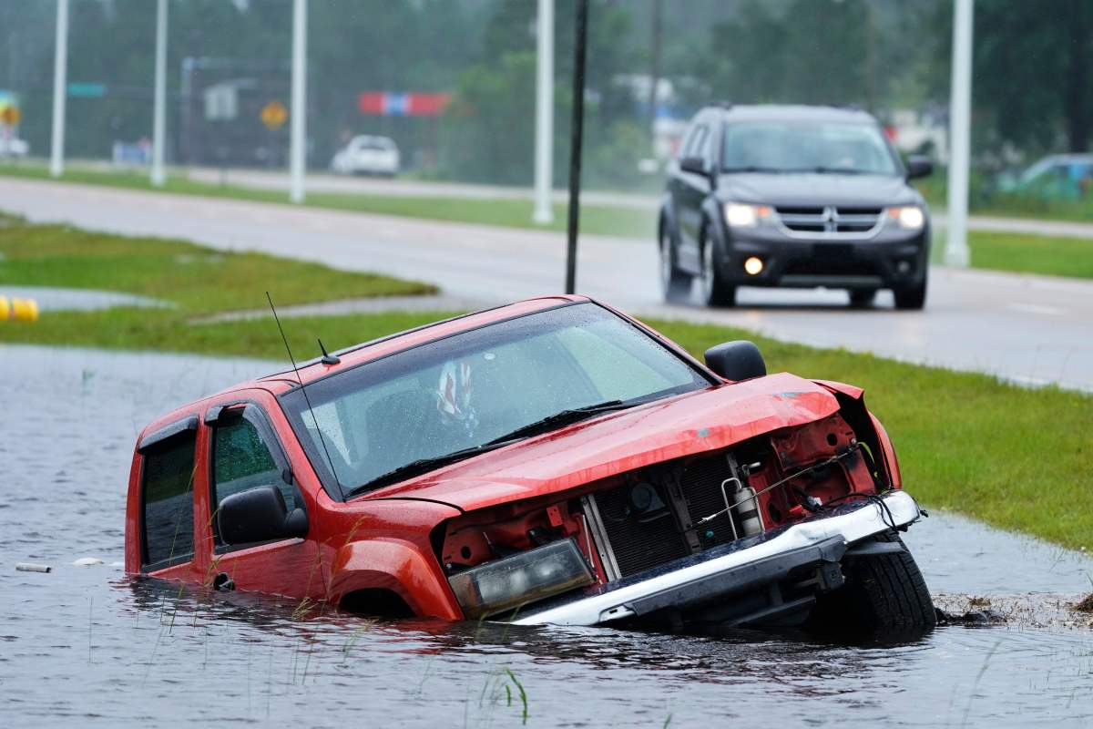 An abandoned vehicle is half submerged in a ditch next to a near flooded highway as the outer bands of Hurricane Ida arrive Sunday, Aug. 29, 2021, in Bay Saint Louis, Miss. (AP Photo/Steve Helber)