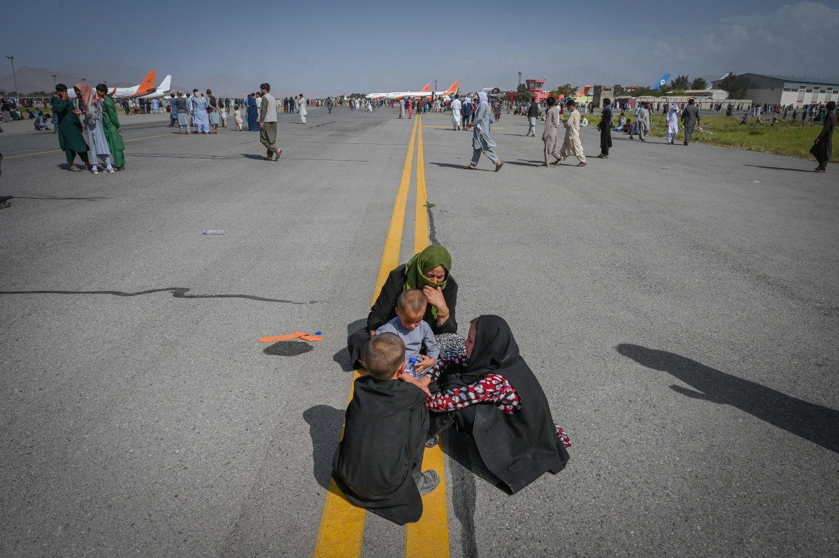 Afghan people sit along the tarmac as they wait to leave the Kabul airport in Kabul on Aug. 16, 2021.