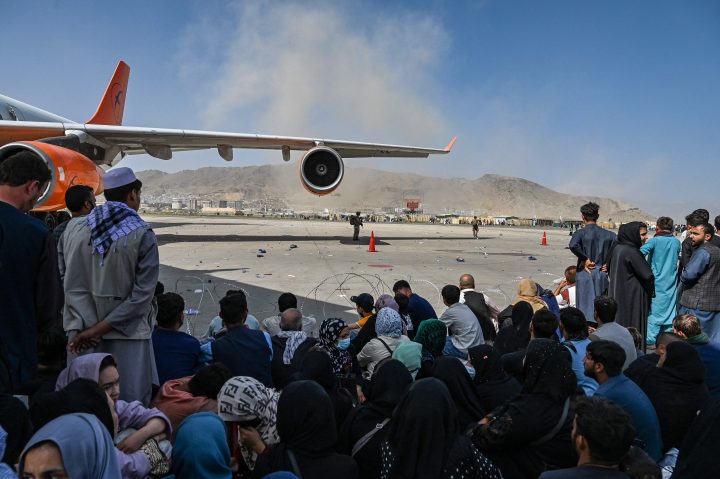 Afghan people sit as they wait to leave the Kabul airport in Kabul on Aug. 16, 2021.