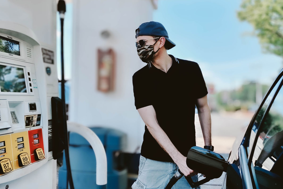 Mid adult man pumps gas wearing protective face mask during COVID-19 pandemic.