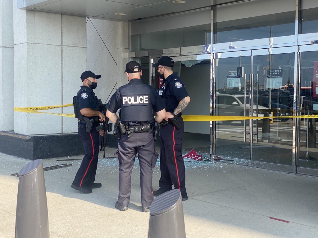 Police officers stand outside Yorkdale Mall after reports of shots fired on Sunday. Shattered glass can be seen behind the officers.
