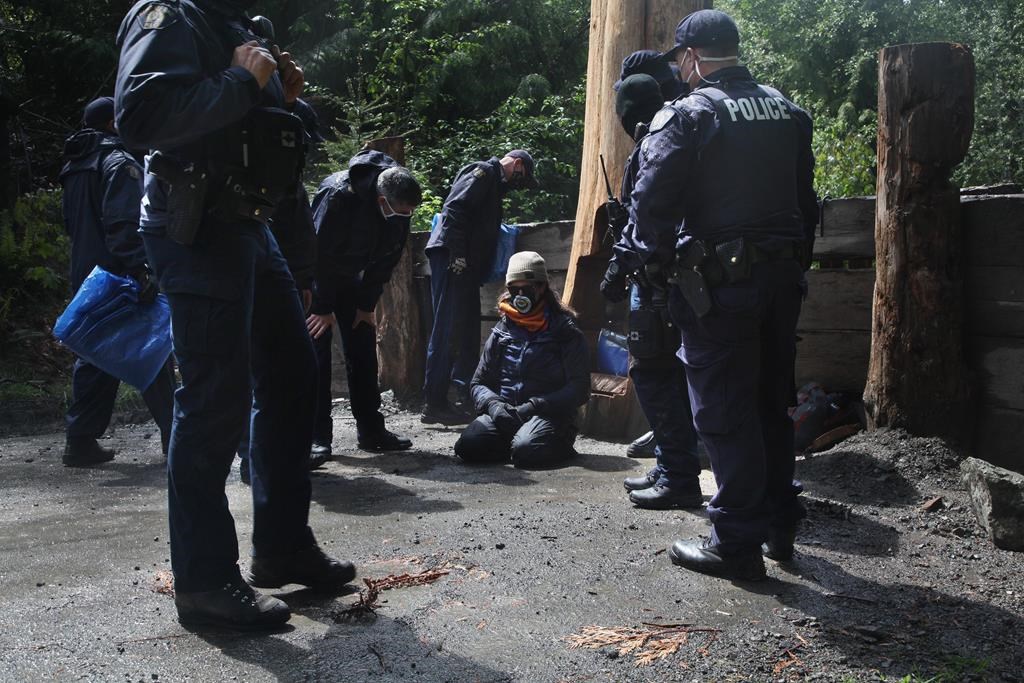 Police speak with a man who calls himself "UDI" after breaking the chain that held him to a stump during an anti-logging blockade in Caycuse, B.C., Tuesday, May 18, 2021. The RCMP's enforcement of a B.C. Supreme Court injunction against blockades set up to prevent old-growth logging on Vancouver Island continued this weekend. THE CANADIAN PRESS/Jen Osborne.