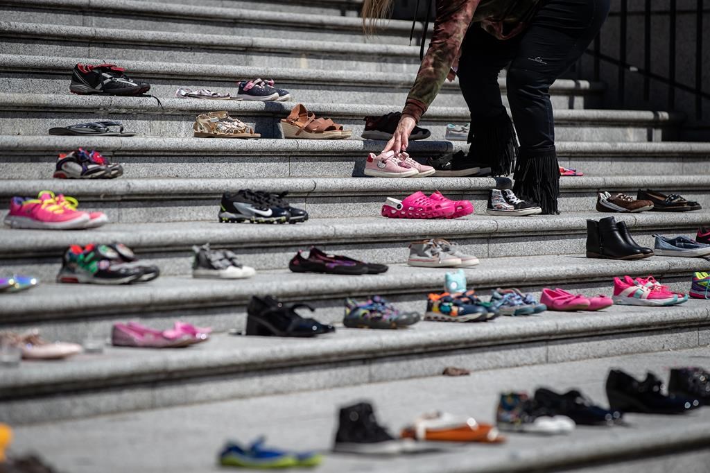 A woman places one of 215 pairs of children's shoes on the steps of the Vancouver Art Gallery as a memorial to the 215 children whose remains have been found buried at the site of a former residential school in Kamloops, in Vancouver, B.C., Friday, May 28, 2021. When the Tk'emlúps te Secwe̓pemc Nation announced the discovery of 215 unmarked graves found at the site of a former residential school in Kamloops, B.C., Canadians had to face the horrific realities Indigenous children and youth had to live while being forced to attend residential schools. THE CANADIAN PRESS/Darryl Dyck.