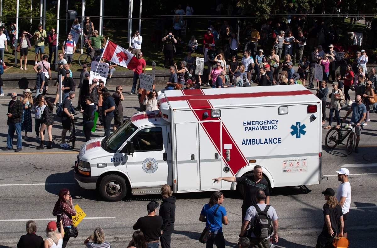 An ambulance passes through a crowd of people protesting COVID-19 vaccine passports and mandatory vaccinations for healthcare workers, in Vancouver, on Wednesday, September 1, 2021. The protest began outside Vancouver General Hospital and police estimated the crowd gathered to be as many as 5,000 people. 