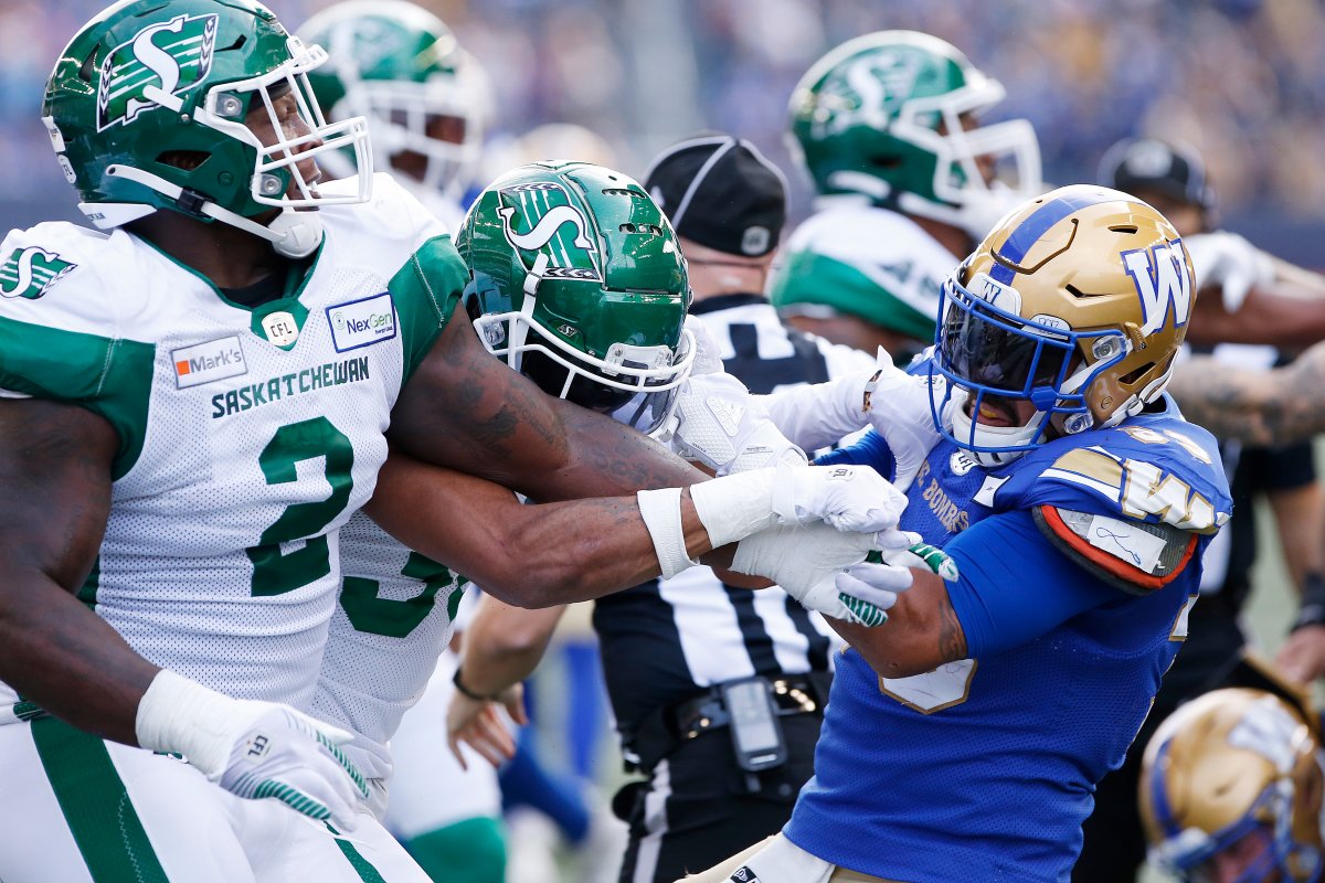 Winnipeg Blue Bombers' Andrew Harris (33) fights with Saskatchewan Roughriders' Micah Johnson (2) and Christian Campbell (38) during first half CFL action in Winnipeg, Saturday, Sept. 11, 2021.
