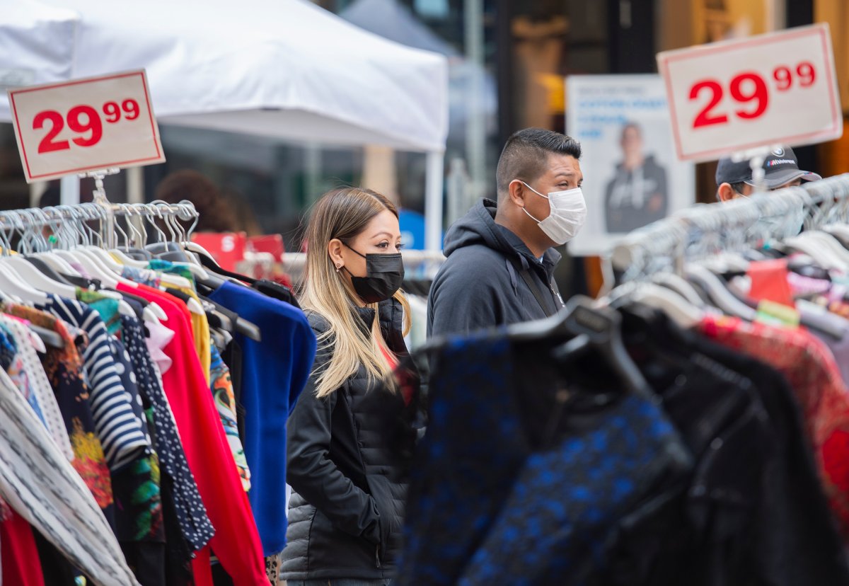 People wear face masks at they walk next to clothing stalls set out for a sidewalk sale on Ste-Catherine Street in Montreal, Sunday, September 12, 2021, as the COVID-19 pandemic continues in Canada and around the world.