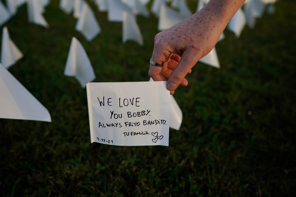Zoe Nassimoff, of Argentina, holds a white flag that is part of artist Suzanne Brennan Firstenberg’s temporary art installation, “In America: Remember,” in remembrance of Americans who have died of COVID-19, on the National Mall in Washington, Friday, Sept. 17, 2021. Nassimoff wrote on the flag in memory of her grandparent who lived in Florida and died from COVID-19. (AP Photo/Brynn Anderson)