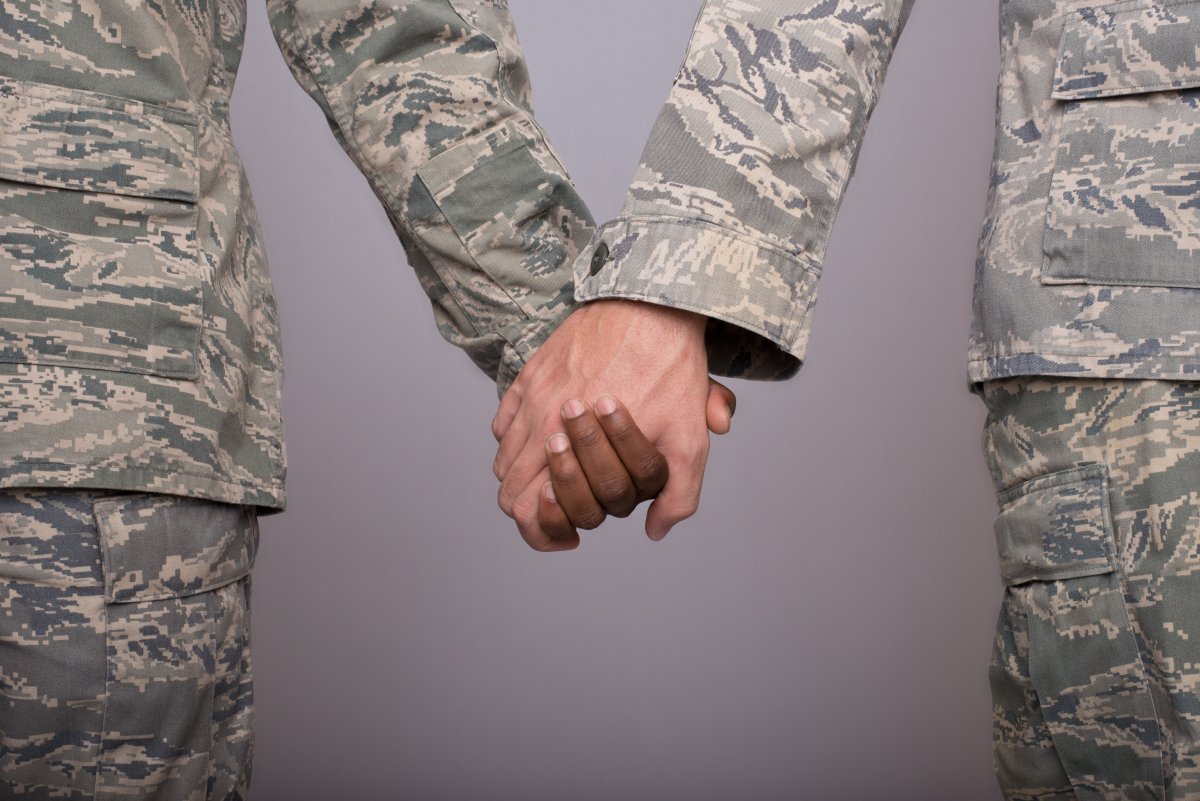 Two military members in uniform hold hands with a gray background.