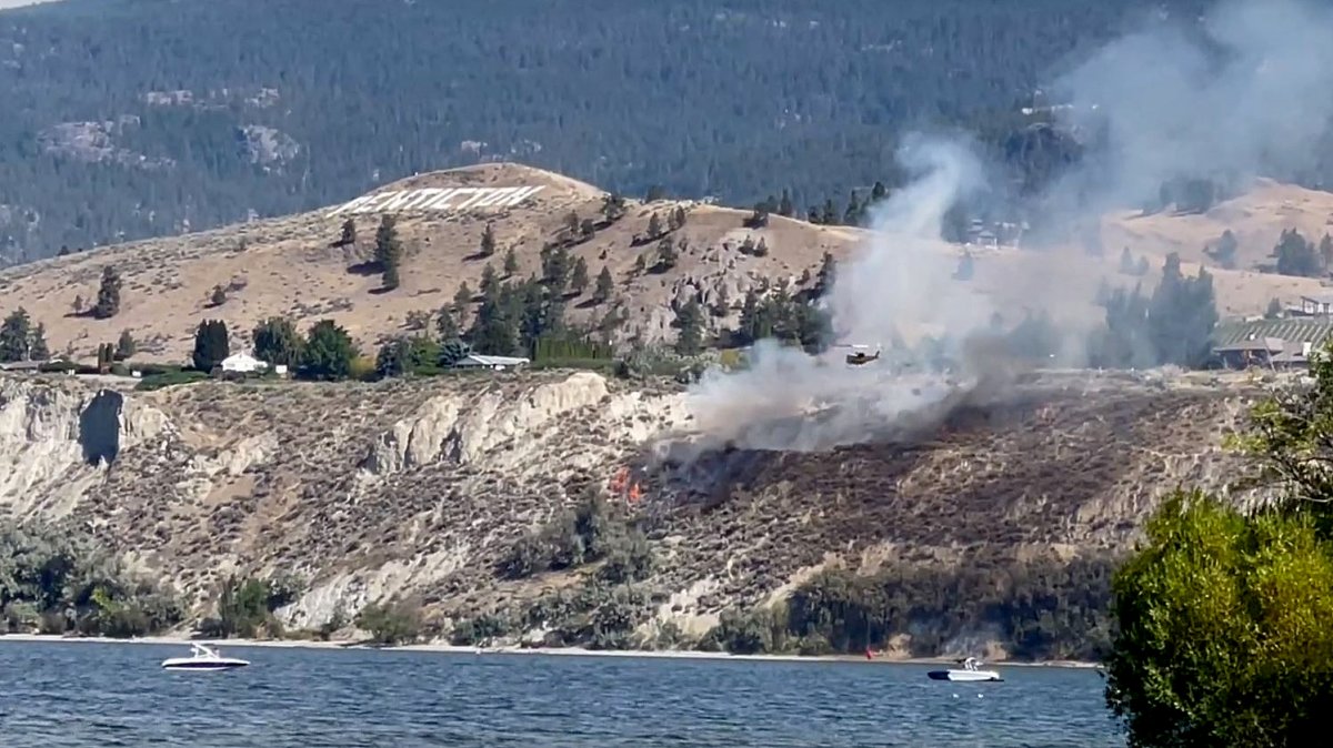 A helicopter is seen bucketing water on a fire burning on a scrub-filled bluff near Penticton.