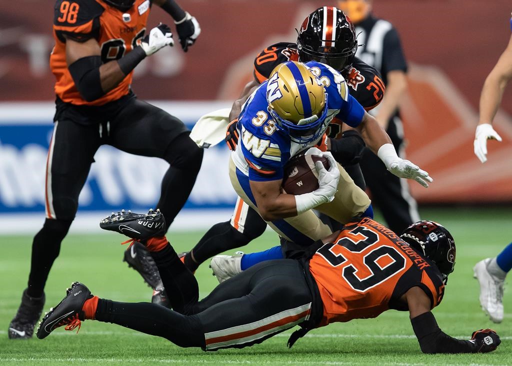 Winnipeg Blue Bombers’ Andrew Harris (33) is tackled by B.C. Lions’ Jalon Edwards-Cooper (29) and Boseko Lokombo (20) during the first half of a CFL football game in Vancouver, on Friday, October 1, 2021. THE CANADIAN PRESS/Darryl Dyck