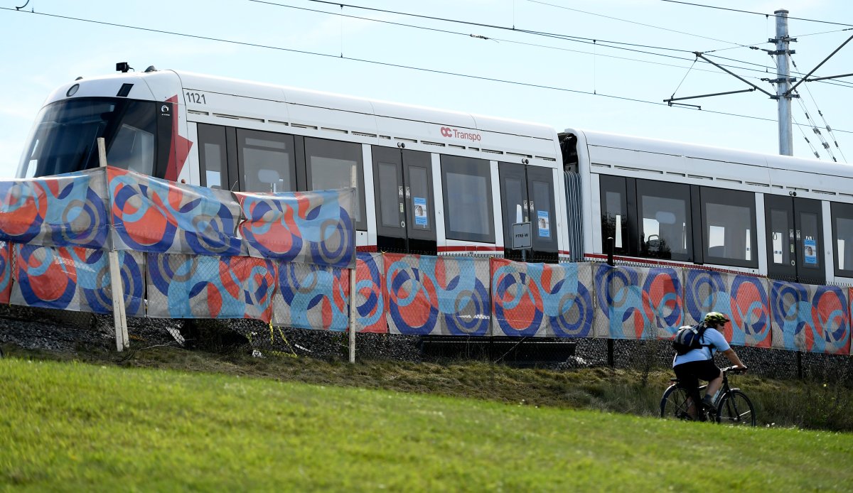 A cyclist rides past a fabric screen placed in front of the segments of an OC Transpo O-Train Monday, Sept. 20, 2021, which derailed west of Tremblay LRT Station in Ottawa.