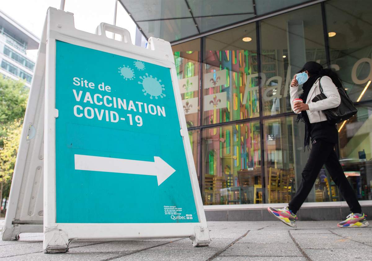 A person removes their face mask as they walk by a sign advertising a COVID-19 vaccination site, in Montreal, Sunday, Oct. 3, 2021. 