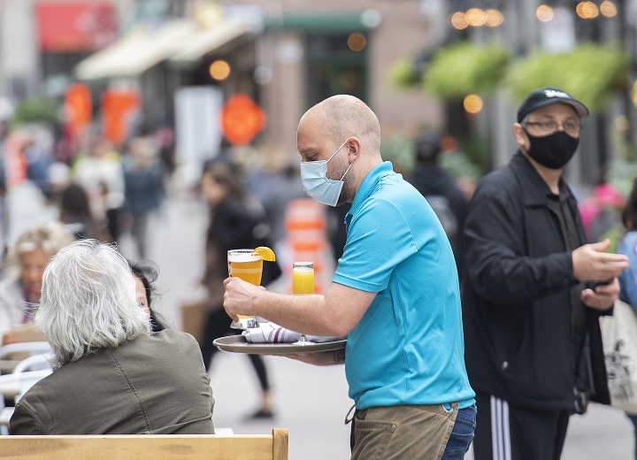 A server wears a face mask as he brings a beer to a customer on an outdoor terrace at a restaurant in Montreal, Sunday, Oct. 3, 2021, as the COVID-19 pandemic continues in Canada and around the world.