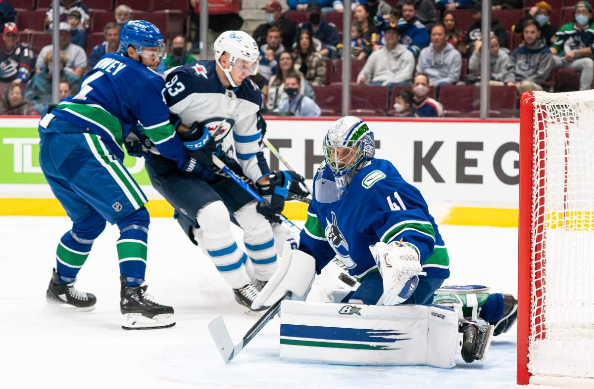 Vancouver Canucks goalie Jarolsav Halak (right) turns away the puck while teammate Madison Bowey (left) ties up Winnipeg Jets’ Kristian Vesalainen during first period NHL pre-season hockey action in Vancouver, Sunday, Oct. 3, 2021.