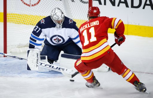 Winnipeg Jets goalie Connor Hellebuyck, left, blocks the net on Calgary Flames’ Mikael Backlund during second-period NHL pre-season hockey action in Calgary.