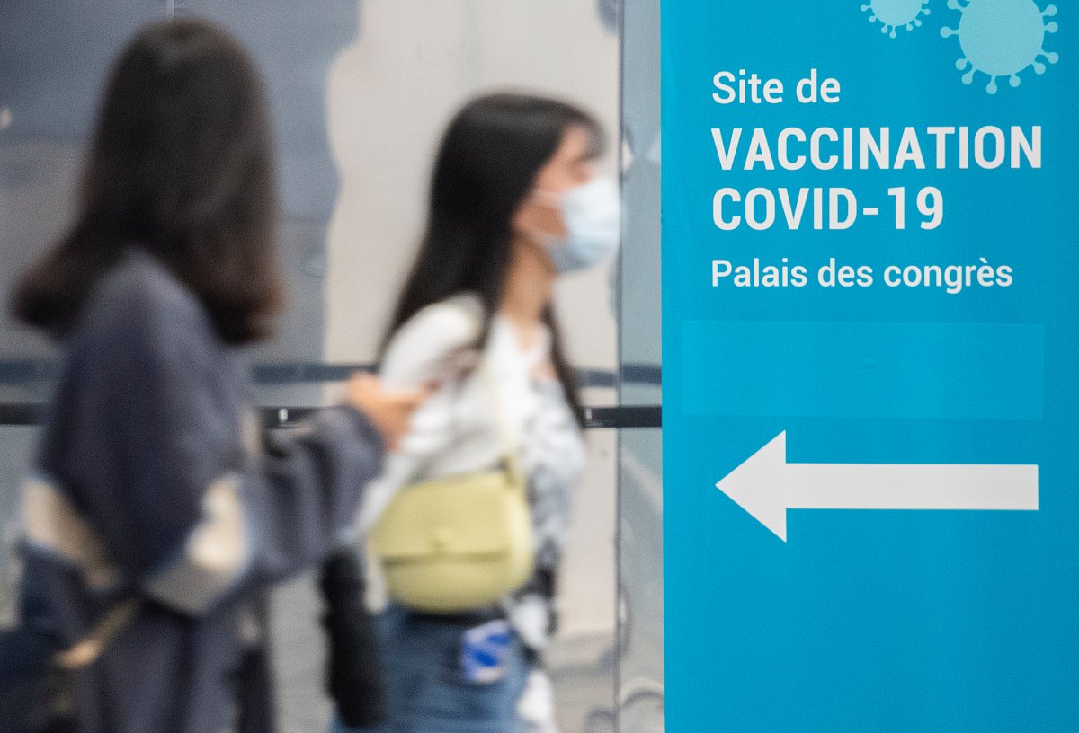 People wear face masks a they walk by a COVID-19 vaccination sign in Montreal, Sunday, October 10, 2021, as the COVID-19 pandemic continues in Canada and around the world. 