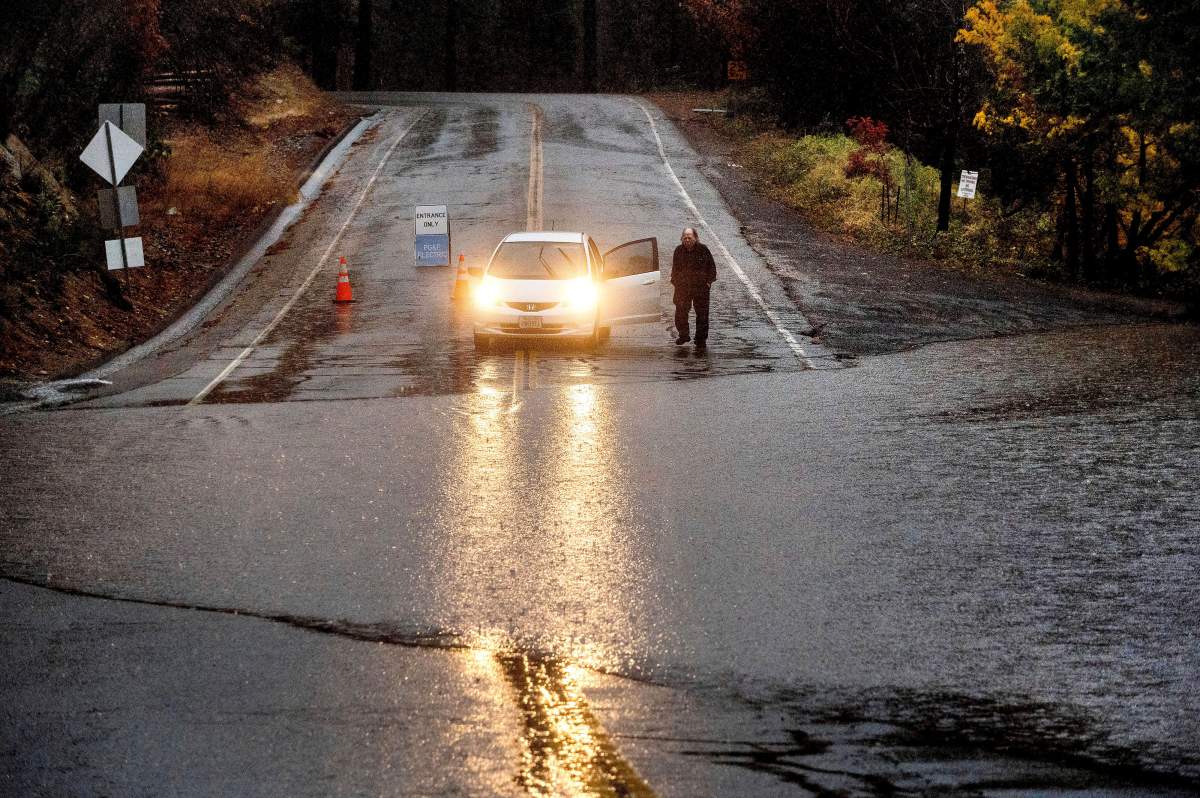 A motorist surveys floodwaters from Lake Madrone crossing Oro Quincy Highway on Sunday, Oct. 24, 2021, in Butte County, Calif. The area burned in 2020’s North Complex Fire.
