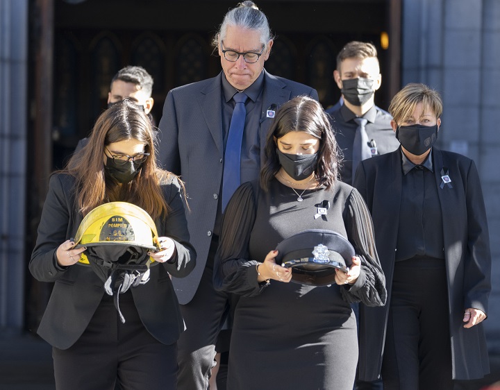 The daughters of fireman Pierre Lacroix, Stephanie and Annick, carry his hat and helmet from the church followed by his brother, Yves Lacroix, after funeral services in Montreal, Friday, Oct. 29, 2021. Lacroix drowned during a rescue operation in the Lachine Rapids last week. 
