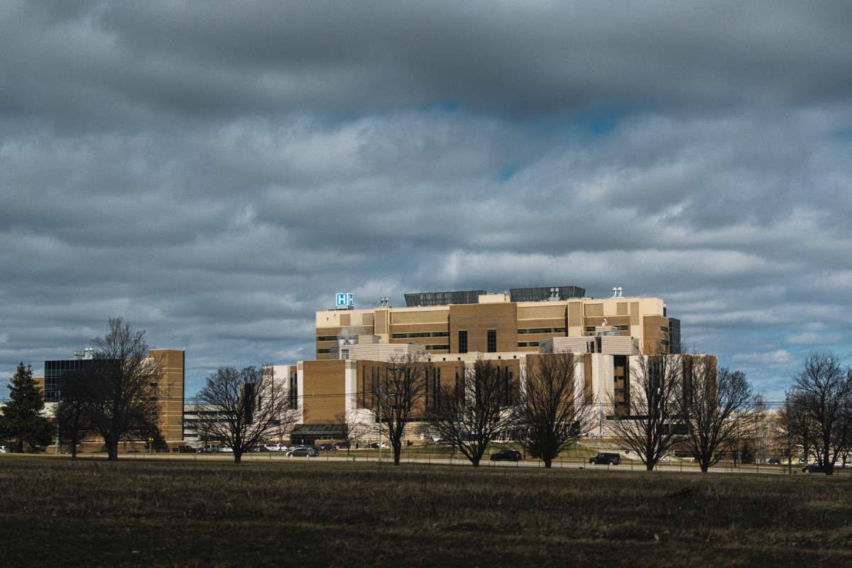 A hospital building seen from a distance under dark clouds.