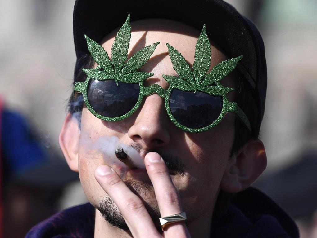 A man smokes a marijuana joint during the annual 4/20 celebration on Parliament Hill in Ottawa, Friday, April 20, 2018. B.C.'s privately-owned cannabis stores can now start stocking pot-themed clothing, books and other goods. THE CANADIAN PRESS/Justin Tang.
