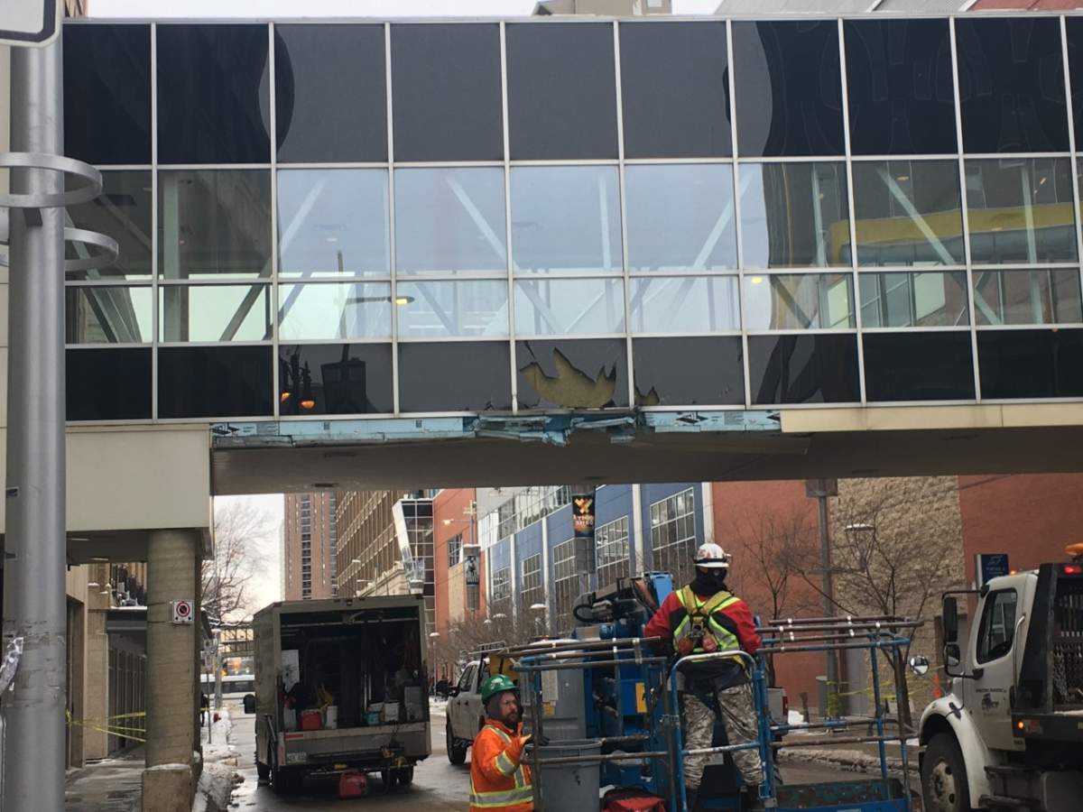 Workers assess the damage after snow clearing equipment hit a skywalk over Donald Street.