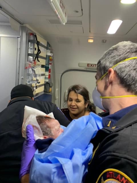 The mom is seen smiling at her baby, which is being held by a firefighter at the back of the plane